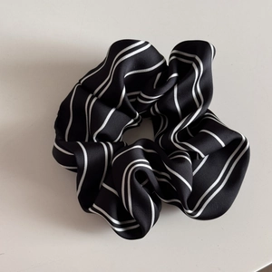 Detail of black striped scrunchie featuring a satin texture and elegant pearl pendant