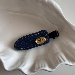 Close-up of denim blue hair clip with gold oval plate on white shell plate
