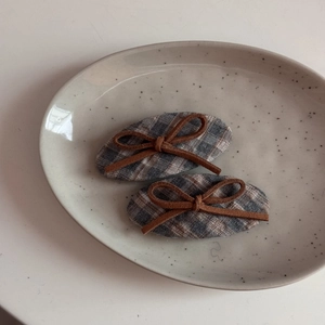 Detail shot of two plaid fabric hair clips with brown bows on a ceramic plate