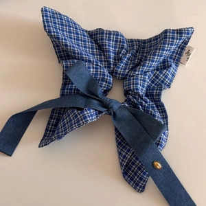 Detail of blue plaid scrunchie with denim bow and golden love charm on white surface