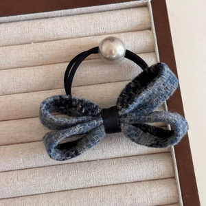 Detailed close-up of blue tweed bow hair tie with silver pearl accent on velvet display