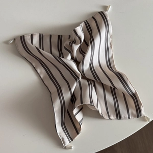 Detailed view of cream silk scarf with black stripes and elegant pearl pendants