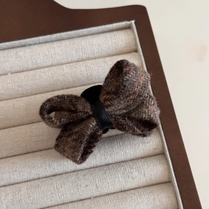Close-up of brown tweed bow hair clip with textured wool fabric and black ribbon