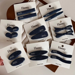 Detail of denim blue hair clips with silver letter tags on white display card