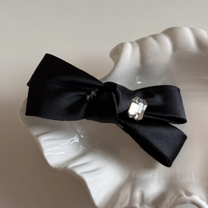 Détail d'une pince à cheveux nœud en soie noire avec cristal brillant sur assiette nacre