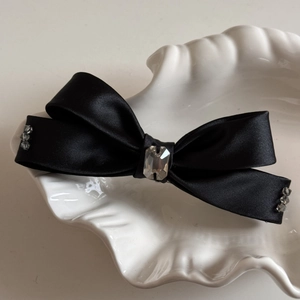 Détail du nœud papillon en satin noir avec cristal étincelant sur un plateau blanc