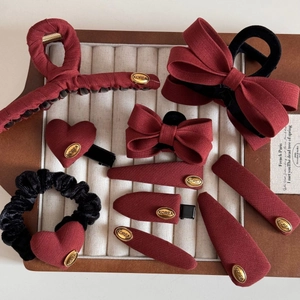 Elegant red and black fabric bow hair clip set with gold metal labels on wood tray