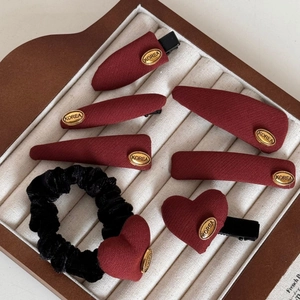 Detailed view of dark red fabric hair clips and black velvet scrunchie in display tray