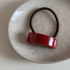 Détail de l'élastique à cheveux rouge en acétate avec étiquette dorée et lien brun