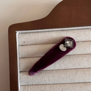 Macro shot of dark purple velvet hair clip with square crystal and silver tag detail