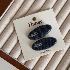 Detailed close-up of blue denim hair clips with silver lettering on display card