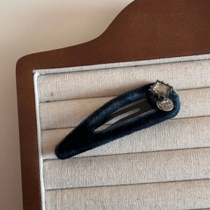 Close-up of velvet blue teardrop hair clip with square rhinestone and metal M charm