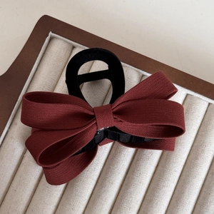 Detail of elegant wine red fabric bow hair clip on a soft velvet display tray