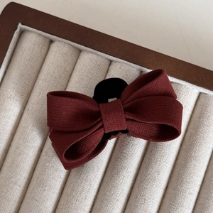 Detailed close-up of textured burgundy bow hair clip on a soft velvet jewelry tray