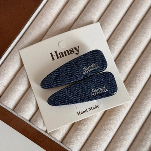 Detailed macro view of denim blue hair clips with silver lettering on soft display cushion