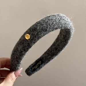 Detail showing grey woolen headband with engraved gold oval buckle and fabric label
