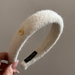 Close-up of beige wool headband with a round gold buckle engraved with Believe in Yourself
