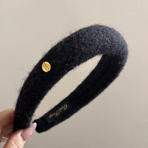 Close-up of black fluffy woolen headband with oval gold buckle and engraved text detail
