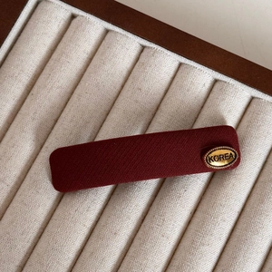 Detail of red knitted fabric hair clip with a gold oval Korea metal tag on a velvet display