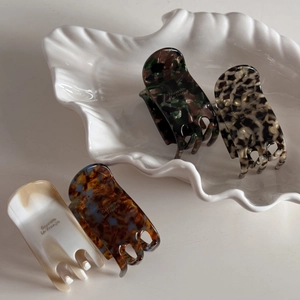 Detail of four assorted acetate claw clips with shell patterns on a ceramic dish