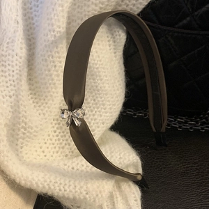 Dettaglio del cerchietto in raso con fiocco di strass su sfondo in maglia bianca