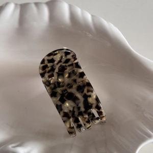 Close-up of acetic acid hair claw with marble texture and golden French lettering detail