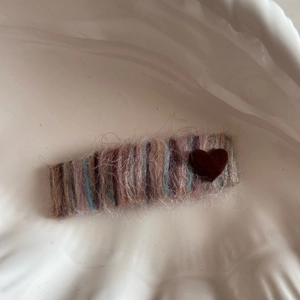 Close-up of knit rainbow hair clip with red heart detail on white textured porcelain