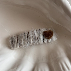 Close-up of wool knitted hair clip with a dark brown heart patch on a white ceramic tray