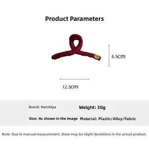 Detail view of burgundy fabric hair claw clip with golden oval logo tag for women