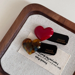 Close-up of heart-shaped hair clips in red and tortoiseshell with handmade gold lettering