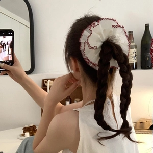Rear view of a model wearing a large white lace scrunchie with red scalloped edges