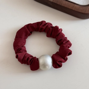 Detail view of a burgundy satin scrunchie with a large white pearl on a white background