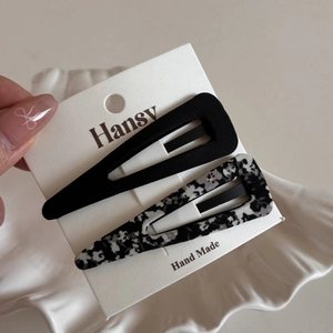 Detail of floral and solid black fabric BB hair clips displayed on a branded white card