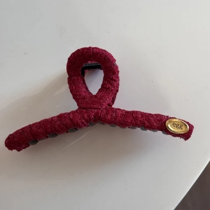 Detail of burgundy tweed fabric wrapped shark hair clip with oval gold metal logo