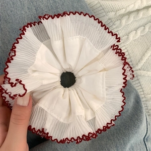 Close-up of a white pleated scrunchie with red merrow edge stitching on hand