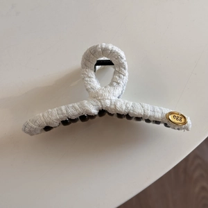 Detail of white woven fabric hair claw clip with golden oval egg metal label