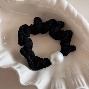 Detail of black ruffled hair scrunchie with large white pearl on shell tray