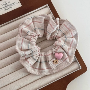 Détail de chouchou vintage à carreaux avec écusson d'ours et cœur sur plateau bijoux