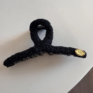 Detail view of the black woven fabric texture and the oval gold metal tag on the hair claw