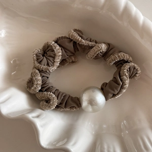 Close-up of brown ruffled hair scrunchie with white plush edges and a large pearl bead