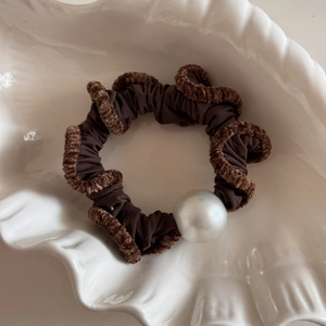 Detail of coffee brown scrunchie with faux fur trim and white pearl on a ceramic tray