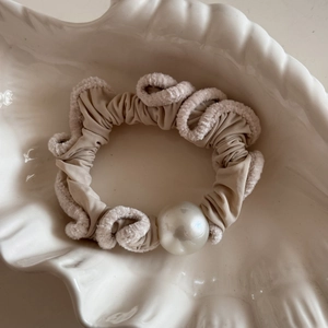 Close-up of beige plush hair scrunchie with soft faux fur edges and elegant pearl detail