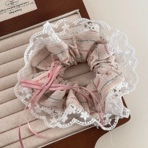 Détail d'un chouchou à carreaux beige avec dentelle blanche et nœud rose en boîte
