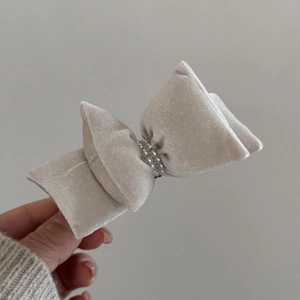 Detail view of a beige velvet bow hair clip featuring elegant double-row pearl embellishments