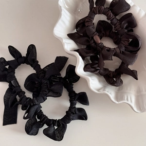 Trois chouchous noirs en tissu plissé avec design à nœuds sur un plateau céramique