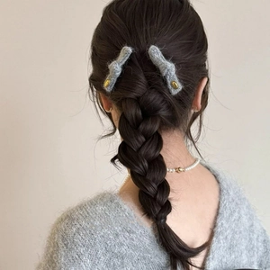Coppia di fermagli per capelli in maglia grigia con etichette dorate su treccia