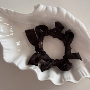 Détail d'un chouchou à nœud noir avec perle marron posé sur un plateau en céramique