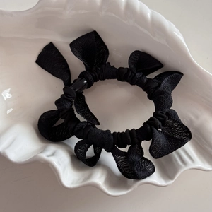 Détail d'un chouchou noir avec nœuds en tissu texturé sur une céramique blanche