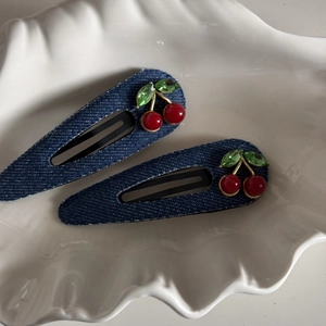 Detailed macro of denim fabric hair clips with red cherry rhinestones and green crystal leaves