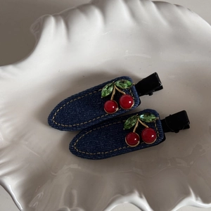 Close-up of denim cherry hair clips with red beads and green rhinestones on white shell tray
